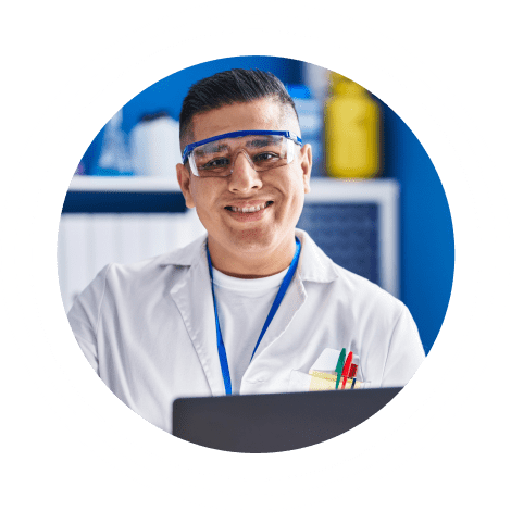 Hombre interno vestido con bata de laboratorio y gafas de seguridad mirando directamente a la cámara y sonriendo.
