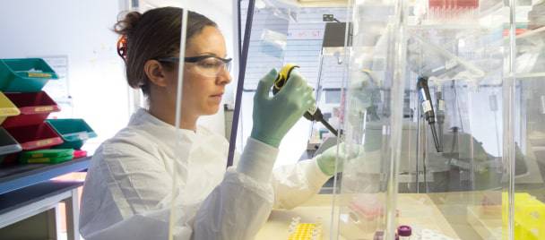 Una becaria del laboratorio Charles River trabajando en el laboratorio con un compañero que la apoya detrás de ella.
