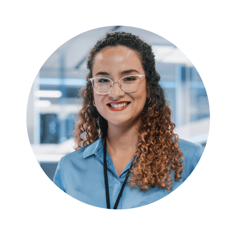 Mujer becaria con gafas de montura blanca de pie en una oficina corporativa vestida con camisa azul abotonada y cordón.
